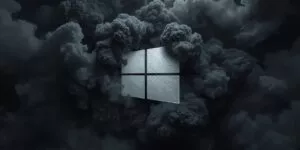 Un'immagine digitale altamente suggestiva e carica di atmosfera che presenta l'iconico logo di Windows fluttuante al centro di una densa e drammatica coltre di nuvole scure. Il logo è reso con una texture materica che ricorda la pietra grezza o il metallo spazzolato di un grigio chiarissimo, quasi bianco, creando un forte contrasto luminoso rispetto allo sfondo. Le nuvole che lo circondano sono volumetrie imponenti e turbolente, simili a fumo denso o a nubi temporalesche, con una colorazione che sfuma dal grigio antracite al nero profondo. La luce sembra provenire dal logo stesso o da una fonte nascosta dietro di esso, illuminando i bordi dei cumuli nuvolosi e conferendo alla scena un senso di profondità tridimensionale e un'aura solenne, quasi cinematografica. L'estetica complessiva è minimale ma potente, con una palette cromatica quasi monocromatica basata su diverse gradazioni di grigio che trasmettono un senso di forza e modernità.