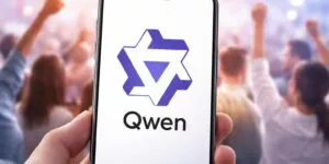 Una immagine che mostra sul monitor di uno smartphone il logo di Qwen e sullo sfondo molte persone che esultano