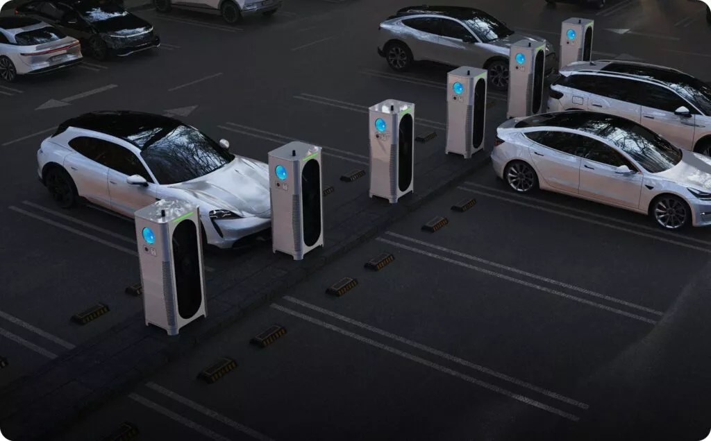 La scena ritrae una stazione di ricarica elettrica durante la notte, con diverse Tesla Model S parcheggiate in fila. Ogni auto è collegata alla rispettiva unità di ricarica, caratterizzata da un design moderno e un'interfaccia digitale. Le stazioni sono illuminate da luci blu e il terreno è segnato da linee bianche per guidare il posizionamento delle vetture. L'area appare ordinata e tranquilla, senza persone o veicoli in movimento, trasmettendo un senso di modernità e consapevolezza ambientale.