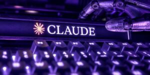 Una mano robotica interagisce con una tastiera meccanica retroilluminata viola; il logo "CLAUDE" si trova su una barra sopra i tasti.