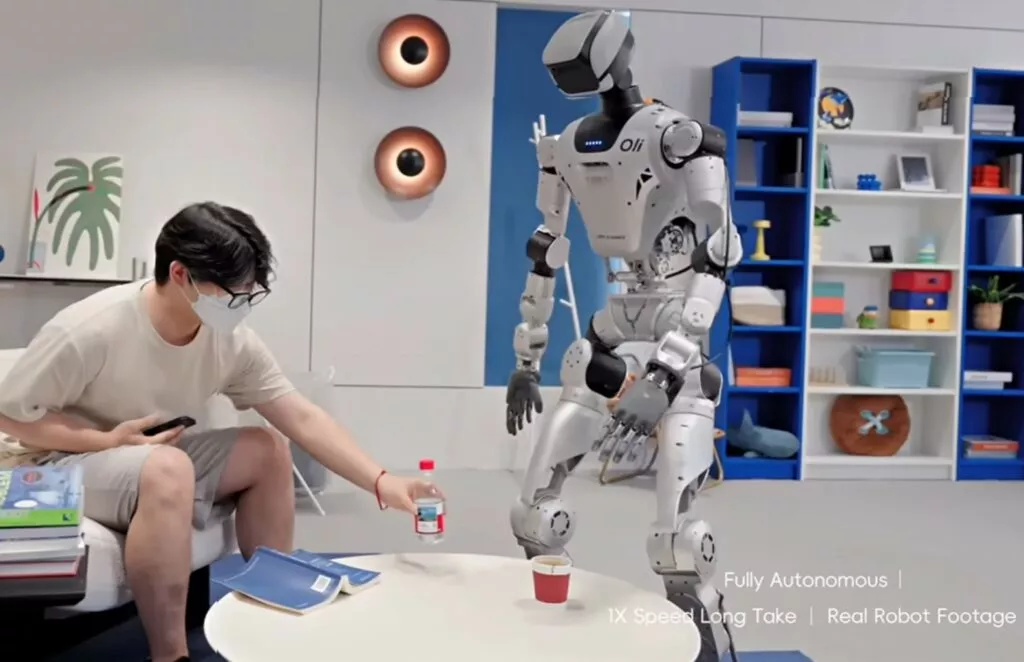 Robot umanoide cinese in stanza da letto pulendo oggetti con agilità, trasportando oggetti senza interruzioni, operando in modo autonome per la pulizia domestica.