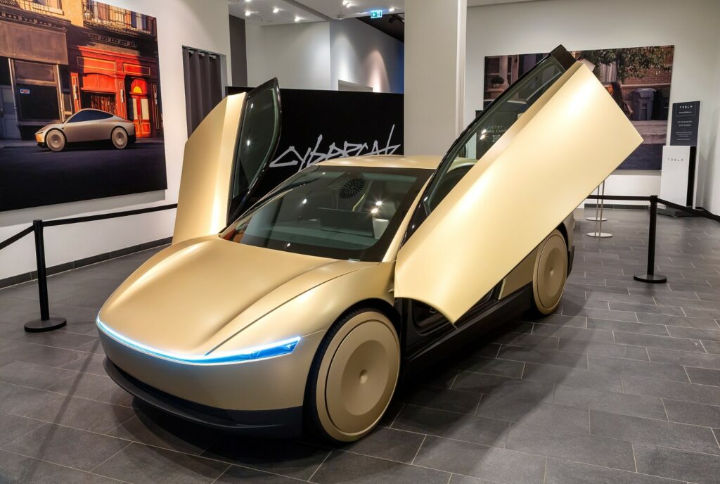 Tesla Cybercab gialla in esposizione con porte aperte, interno moderno, in un salone. Foto realizzata da https://commons.wikimedia.org/wiki/User:Avda