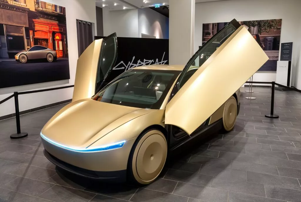 Tesla Cybercab gialla in esposizione con porte aperte, interno moderno, in un salone. Foto realizzata da https://commons.wikimedia.org/wiki/User:Avda
